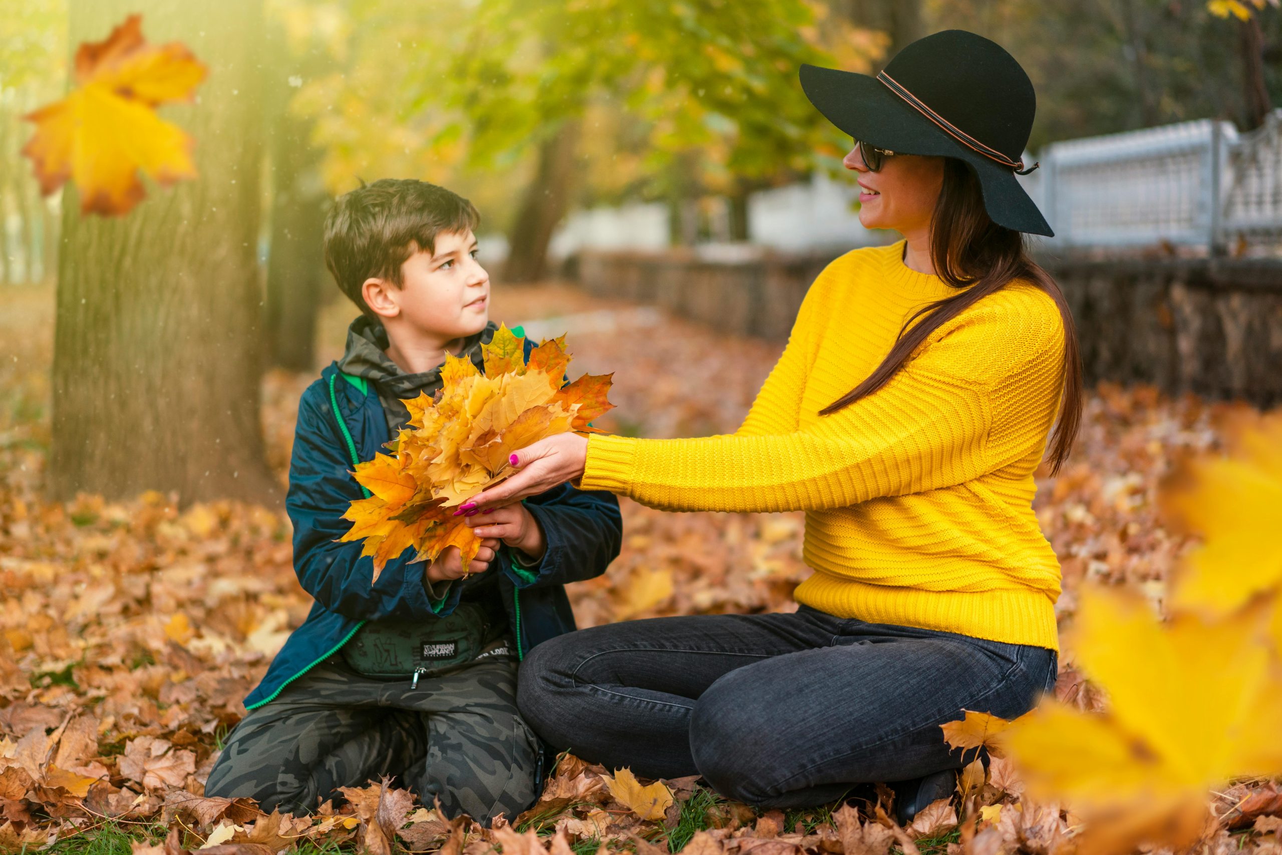 A mother and her son enjoy a playful moment with leaves during a fall day in the park.