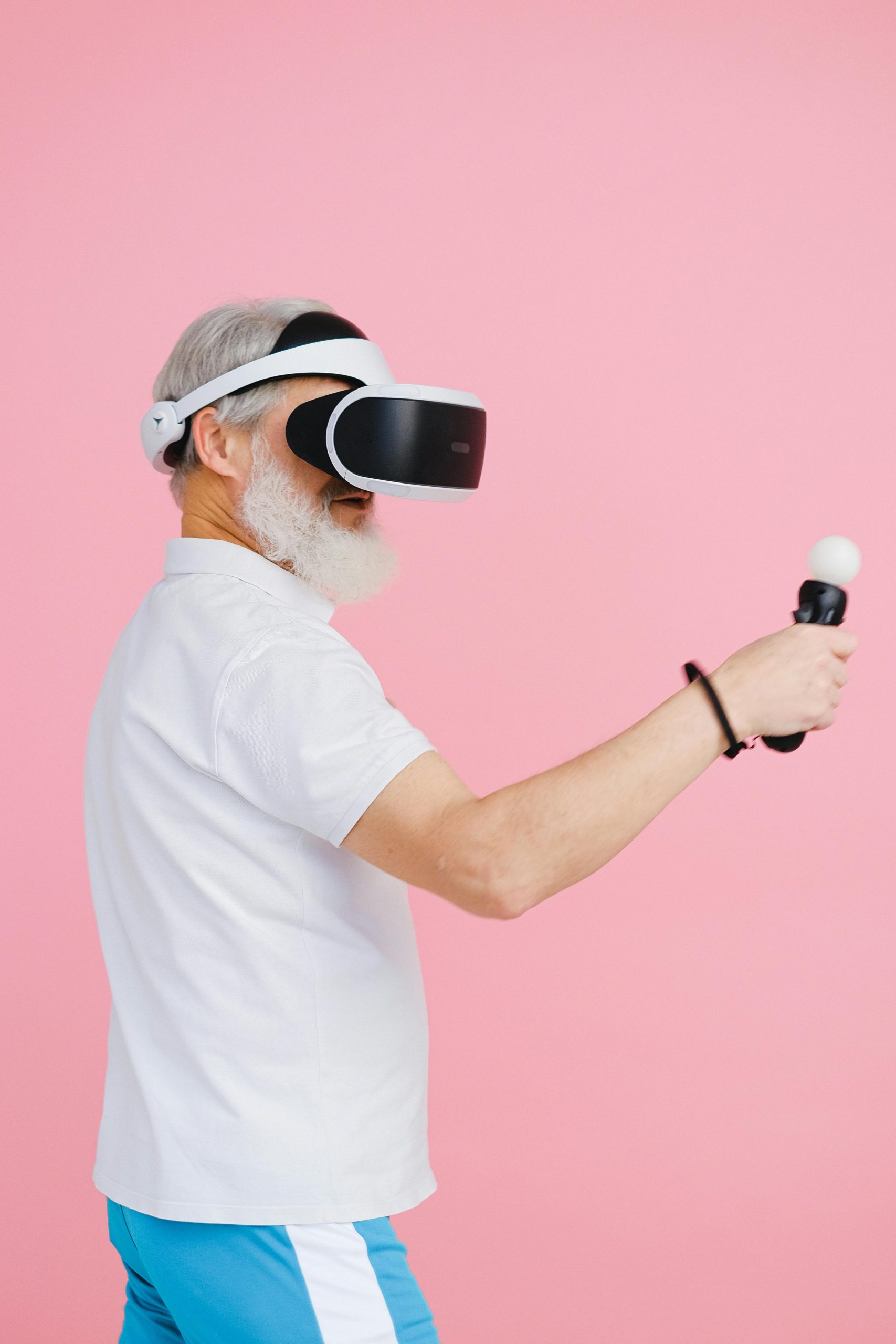 Elderly man using VR headset and controller on pink background.